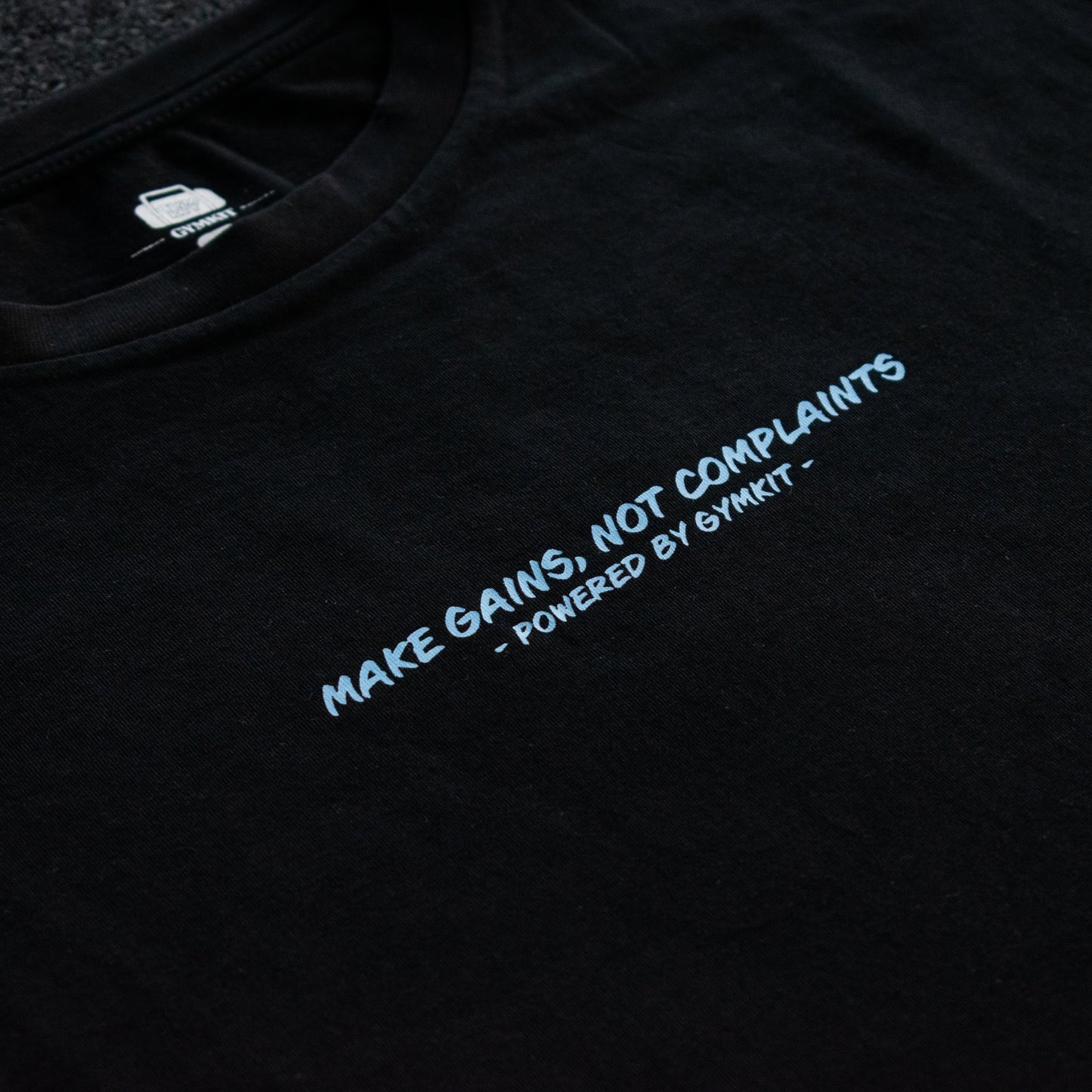 Black t-shirt with white text 'MAKE GAINS, NOT COMPLAINTS' on a dark background