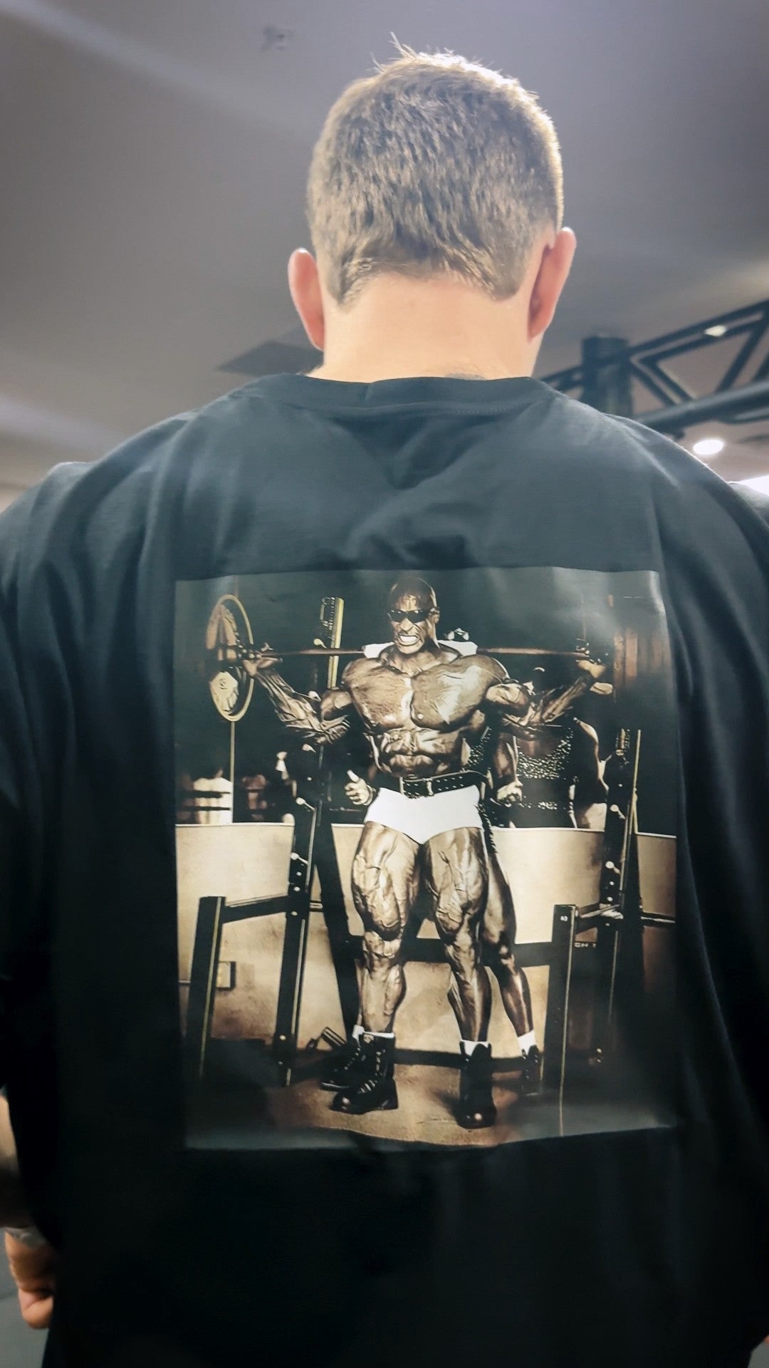 Person wearing a black t-shirt with a vintage-style graphic of a muscular figure on the back.
